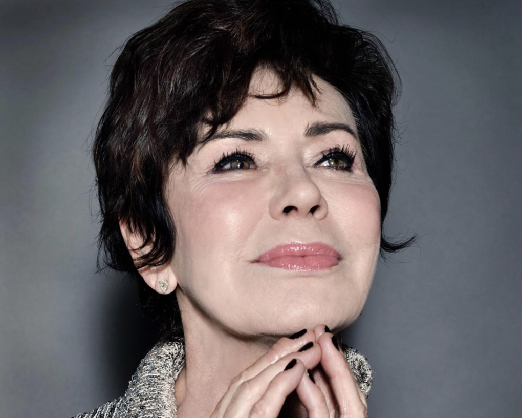 Ritratto recente in studio di Corinne Cléry, capelli corti scuri, mani sotto il mento e sguardo verso l'alto