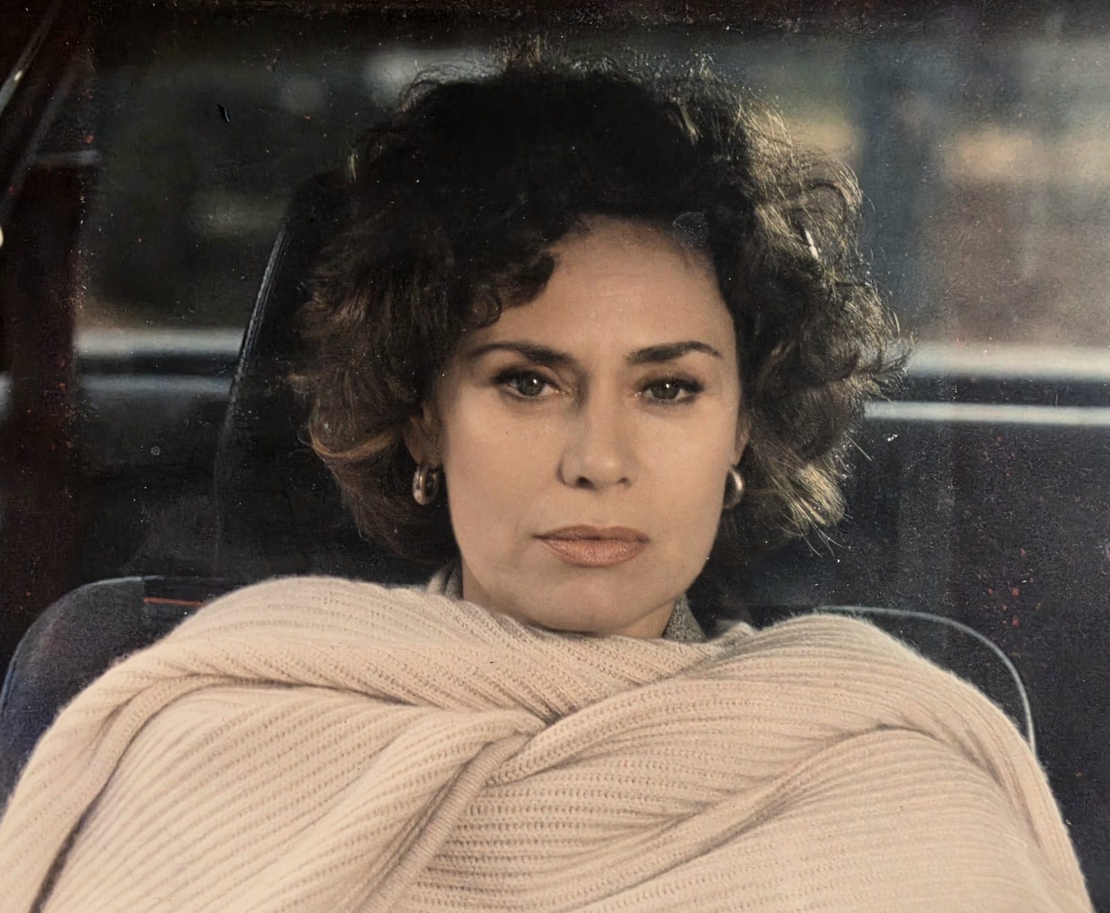 Corinne Cléry a colori in una foto di scena degli anni Ottanta, seduta in auto avvolta in uno scialle chiaro